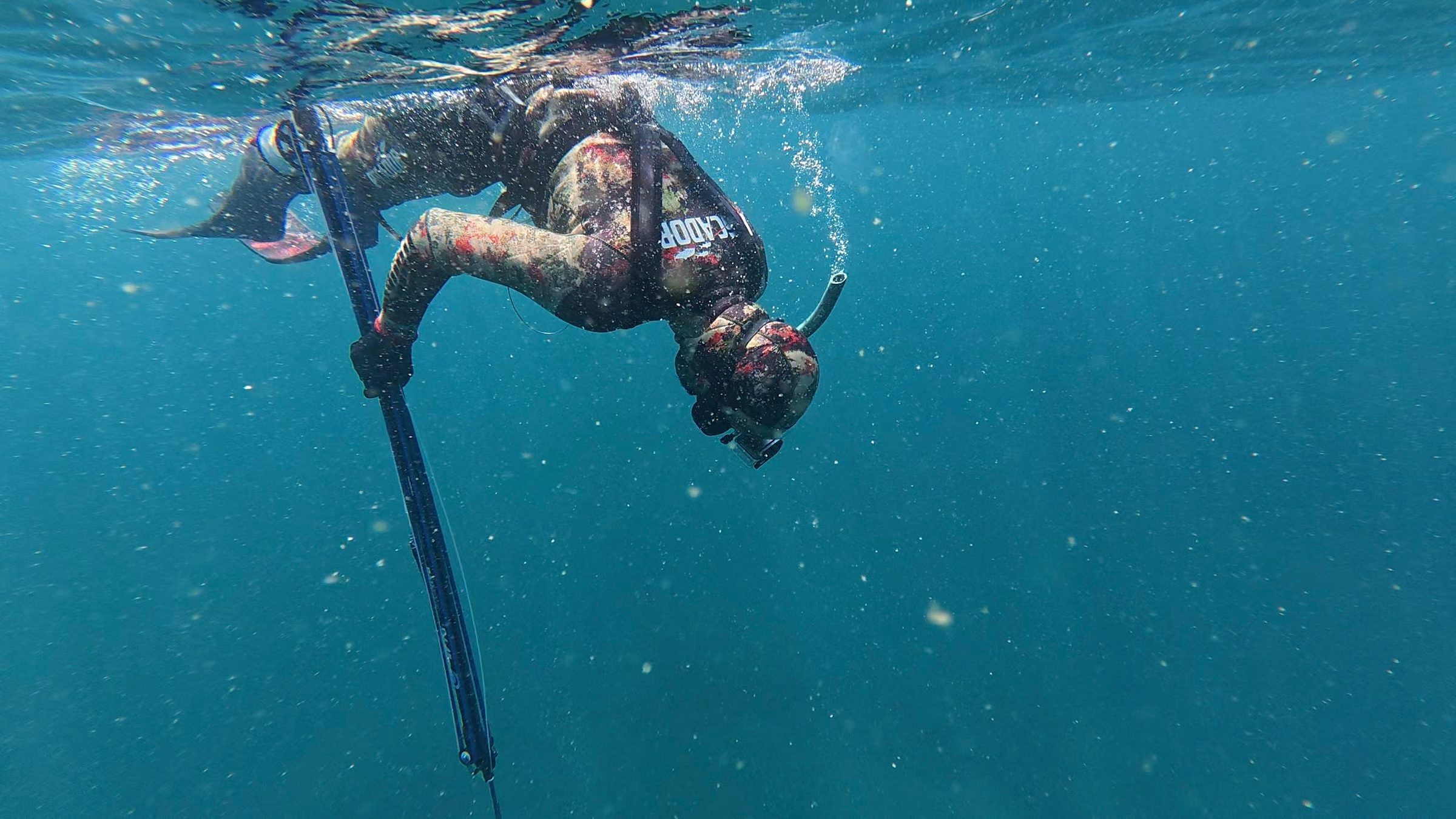 Sameer Ahmed Khan duck-diving below the surface in a camouflage wetsuit, speargun in hand, in the Arabian Sea